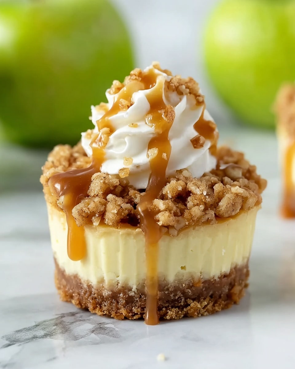 A small round dessert with three clear layers sits on a white marbled surface. The bottom layer is a chewy crumbly brown crust. The middle layer is smooth, creamy, and pale yellow in color. The top layer is a rough textured crumbled mixture in light brown tones, with visible small nut pieces. On top of this, there is a dollop of white whipped cream with glossy caramel sauce drizzled over it. In the background, blurry green apples can be seen, adding a fresh accent. photo taken with an iphone --ar 4:5 --v 7
