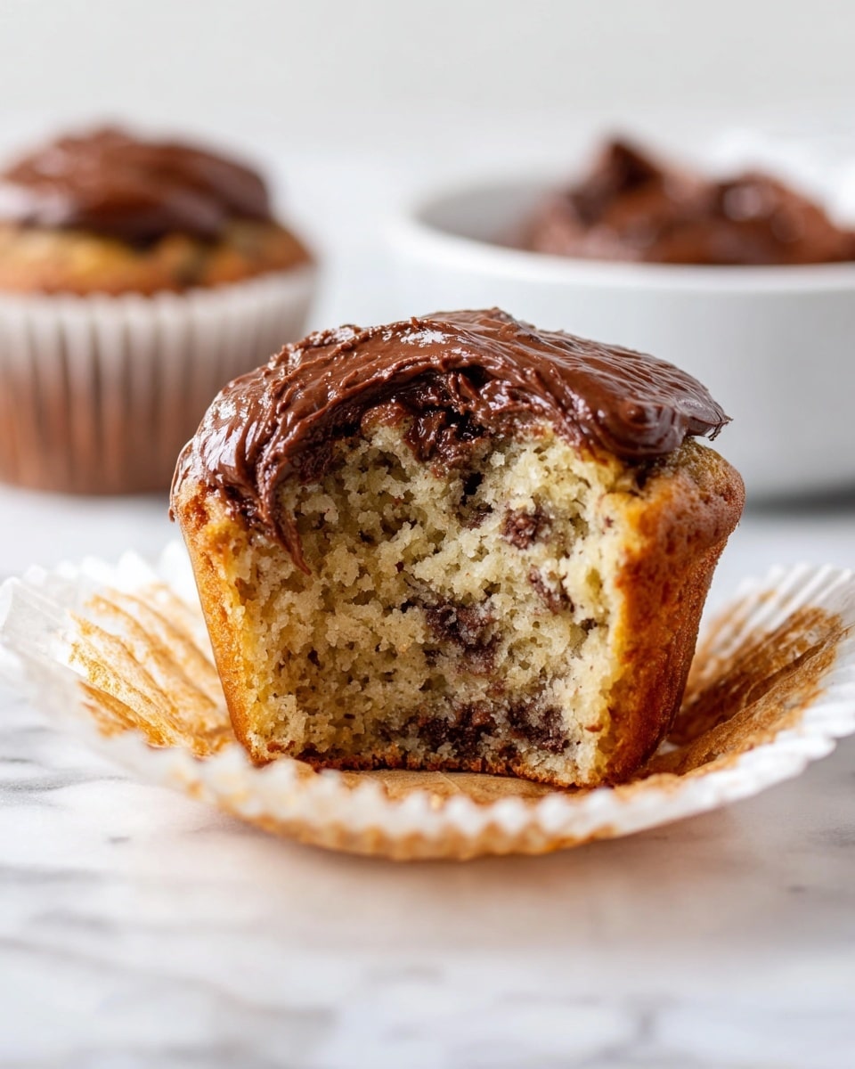 A close-up view of a single muffin wrapped in a white paper liner, showing a golden-brown base with a slightly rough texture. The top layer is uneven with melted chocolate swirls and spots that create a glazed look, giving a mix of light brown and darker chocolate brown colors. The muffin rests on a white marbled surface, bright and clean in the background. photo taken with an iphone --ar 4:5 --v 7