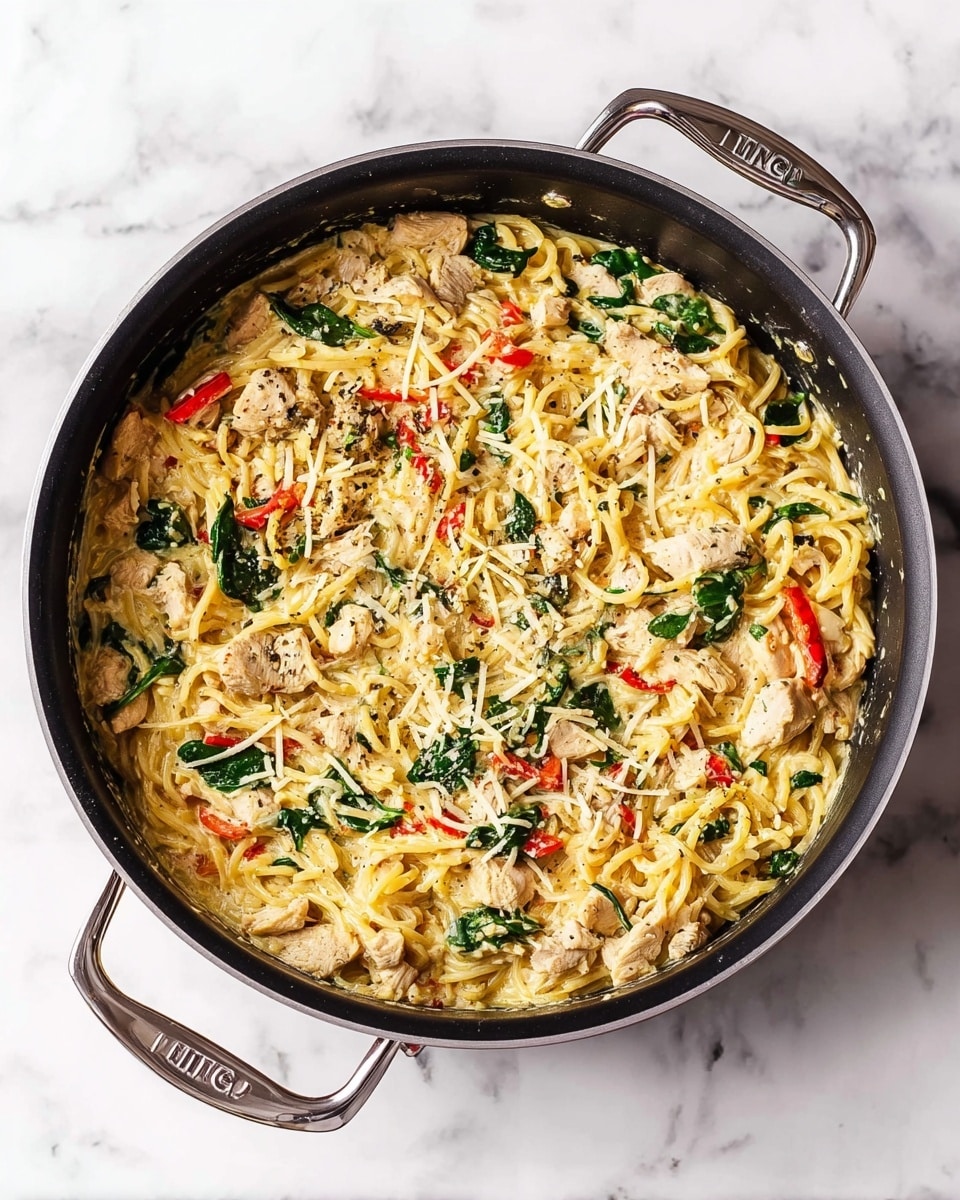 A black frying pan filled with a creamy pasta dish sits on a white marbled surface. The dish shows two main layers: the base is creamy, light yellow sauce mixed with small pieces of cooked chicken that are light brown with pepper specks. Scattered throughout are bright green spinach leaves and thin strips of red bell pepper, adding color contrast. Shredded cheese is lightly melted and spread unevenly on top, blending with the sauce. The pan has two silver handles on each side with the brand's name visible. photo taken with an iphone --ar 4:5 --v 7