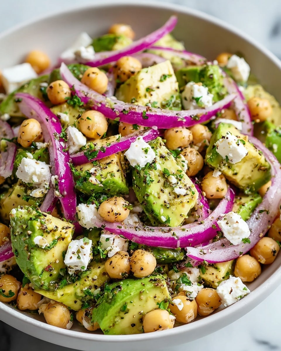 A white bowl filled with a fresh salad made of three main layers: at the bottom, golden round chickpeas spread evenly; in the middle, green avocado slices placed closely together showing their creamy texture; on top, scattered thin rings of purple-red onion and crumbled white cheese chunks. The salad is sprinkled with finely chopped green herbs and specks of black pepper. A silver spoon rests inside the bowl, with the salad looking fresh and colorful on a white marbled surface photo taken with an iphone --ar 4:5 --v 7