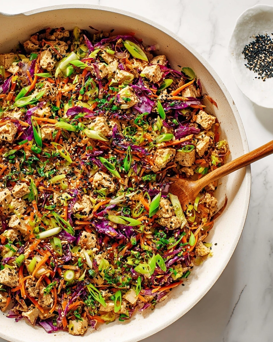 Large white ceramic skillet filled with a vibrant tofu stir-fry, featuring crumbled tofu, finely shredded purple and green cabbage, julienned carrots, and chopped scallions, all tossed together with a sprinkling of black and white sesame seeds, the whole dish shown from a close 3/4 angle on a white marble countertop with natural lighting, styled as a professional food magazine hero shot, photo taken with an iphone --ar 4:5 --v 7