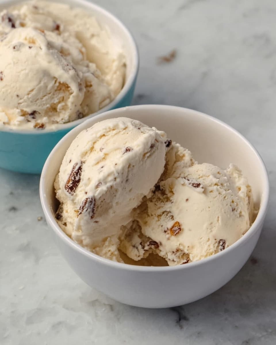 A white bowl filled with three scoops of light beige ice cream with small brown nut pieces mixed throughout, placed on a white marbled surface. In the background, there is a jar with a wooden honey dipper resting beside it and a soft white cloth partially visible. The scene is softly lit, showing the creamy texture of the ice cream clearly. photo taken with an iphone --ar 4:5 --v 7