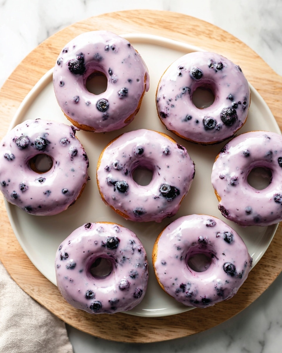 A white platter showcasing a full batch of six freshly baked blueberry donuts, each evenly coated with a smooth, lavender-colored glaze speckled with bits of real blueberries, arranged in a neat circle on a natural light wooden board, capturing the entire assortment from a professional 3/4 angle shot on a white marble countertop, styled for a food magazine hero shot, natural lighting enhancing the soft textures and vibrant colors, photo taken with an iphone --ar 4:5 --v 7