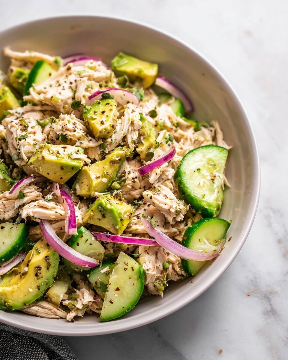 Large white bowl filled with a vibrant salmon avocado salad featuring chunky pieces of tender salmon, ripe avocado slices, bright cucumber chunks, and thin rings of crisp red onion, all lightly seasoned with cracked black pepper, beautifully arranged to showcase freshness and texture, shot from a 3/4 angle on a white marble surface with natural lighting, styled as a hero food magazine photograph, photo taken with an iphone --ar 4:5 --v 7