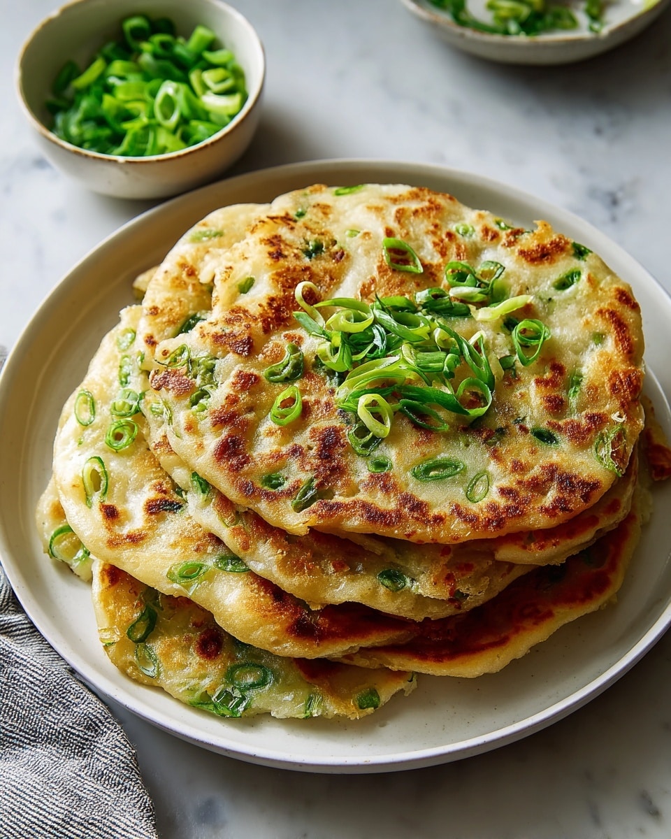 White serving plate stacked with a generous pile of golden-brown scallion pancakes, each pancake speckled with vibrant green sliced scallions and cooked to a crispy texture, alongside a small white bowl filled with fresh chopped scallions as garnish, entire dish presented on a white marble countertop with natural lighting, professional food magazine style hero shot photographed with an iphone --ar 4:5 --v 7