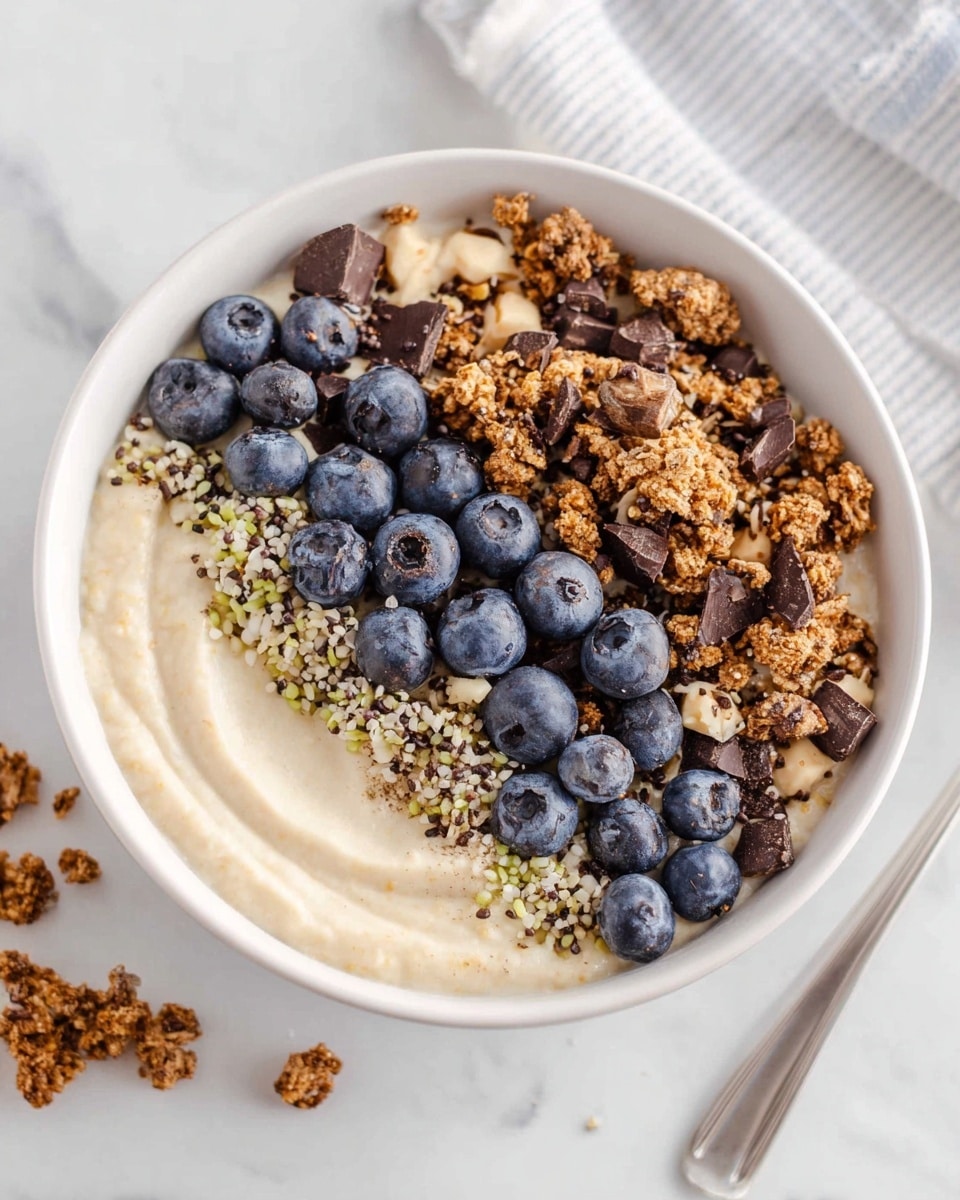 Large white bowl filled with a creamy smoothie base topped with layers of crunchy granola, a generous row of fresh blueberries, sprinkled cacao nibs, and hemp seeds, arranged in neat sections covering the entire surface, multiple similar bowls arranged nearby, all set on a white marble countertop under soft natural lighting, professional food magazine style hero shot photographed with an iphone --ar 4:5 --v 7