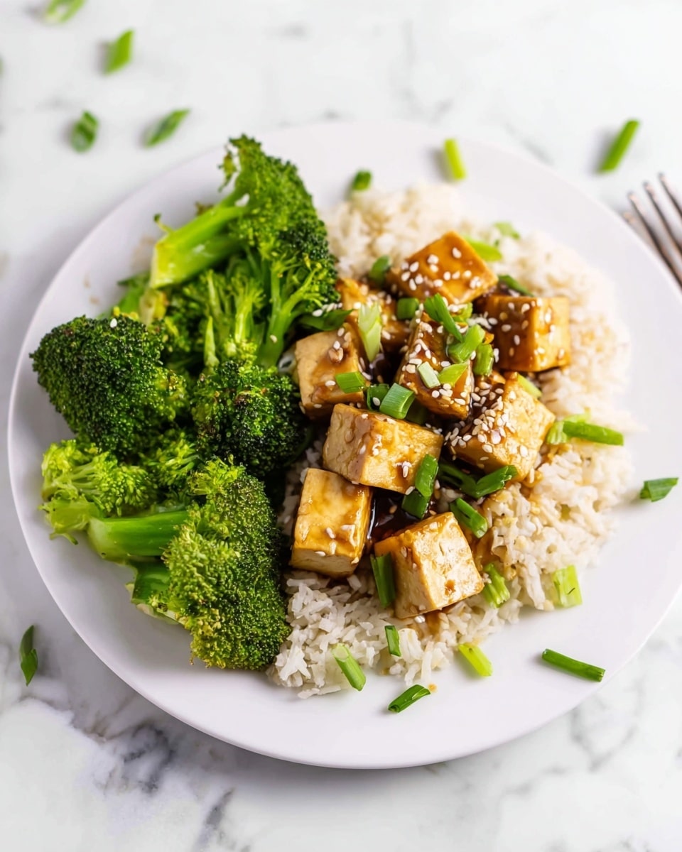 Large white serving bowl filled with generous portions of tofu and steamed broccoli florets, served over a bed of fluffy brown rice, tofu cubes glazed with a glossy savory sauce and sprinkled with sesame seeds and chopped green onions, whole dish captured from a 3/4 angle on a white marble countertop with natural light, styled as a professional food magazine hero shot, photo taken with an iphone --ar 4:5 --v 7