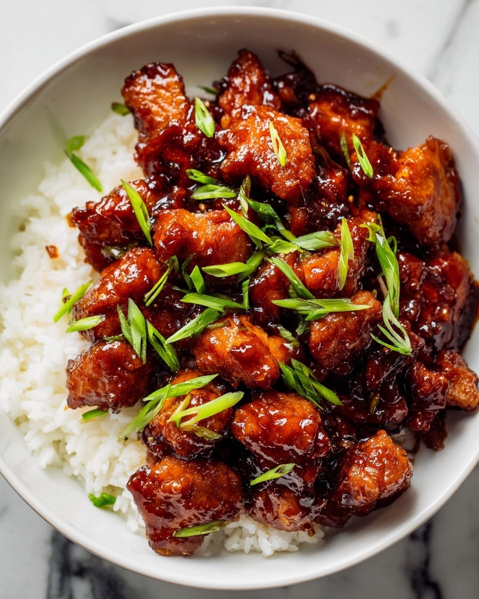 Large white bowl filled with a generous serving of sticky glazed orange chicken chunks, glistening with rich sauce, served over a bed of fluffy steamed white rice and garnished with freshly sliced green onions, photographed from a professional 3/4 angle on a white marble countertop under natural lighting, whole dish in frame, food magazine hero shot style photo taken with an iphone --ar 4:5 --v 7