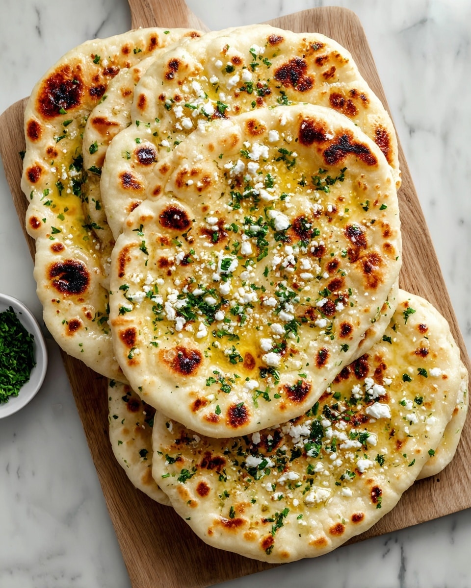 A stack of five whole naan breads on a large white rectangular platter, each naan brushed with golden melted butter, sprinkled with crumbled white cheese and finely chopped fresh herbs, arranged neatly to showcase their fluffy, slightly charred texture, set against a white marble countertop with natural lighting, styled like a food magazine hero shot, photo taken with an iphone --ar 4:5 --v 7