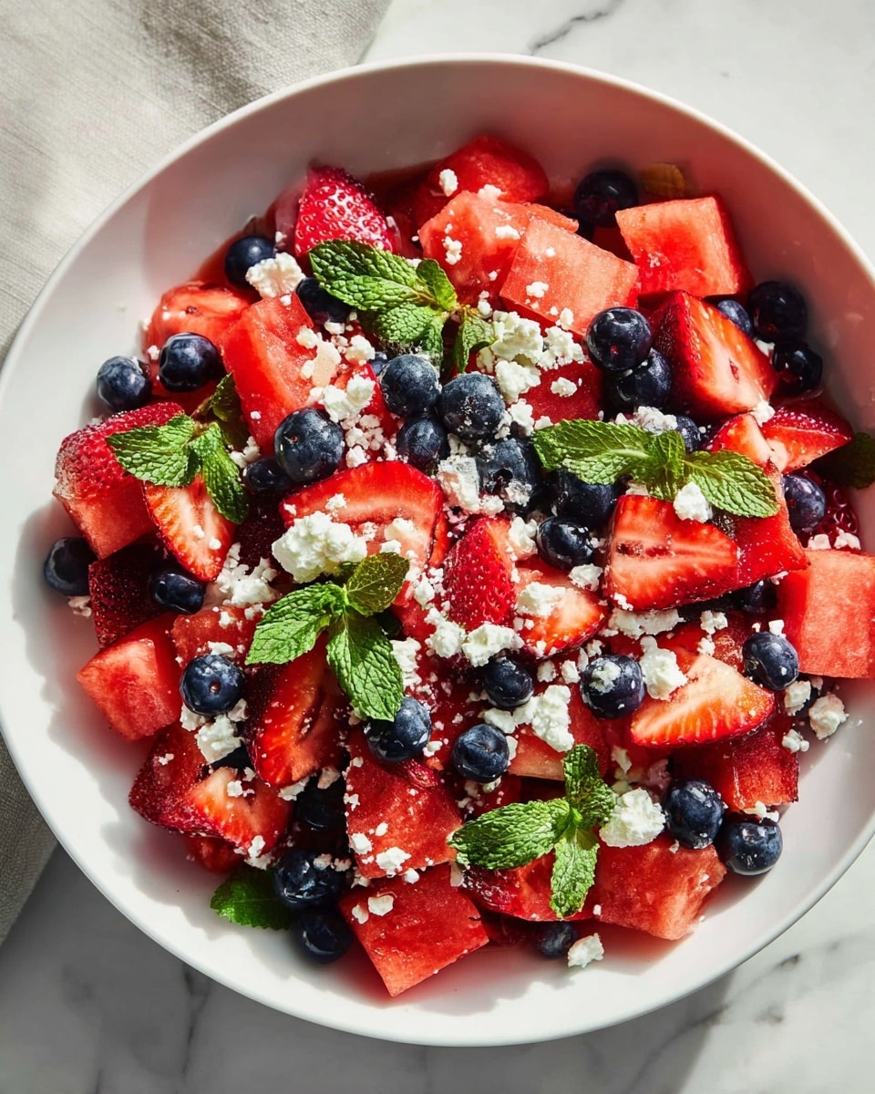 Large white bowl filled with a vibrant, fresh watermelon salad featuring whole blueberries, sliced strawberries, chunks of watermelon, sprinkled with crumbled white cheese and garnished with bright green mint leaves, the whole dish displayed beautifully on a white marble countertop with natural lighting, professional overhead food magazine style photo taken with an iphone --ar 4:5 --v 7