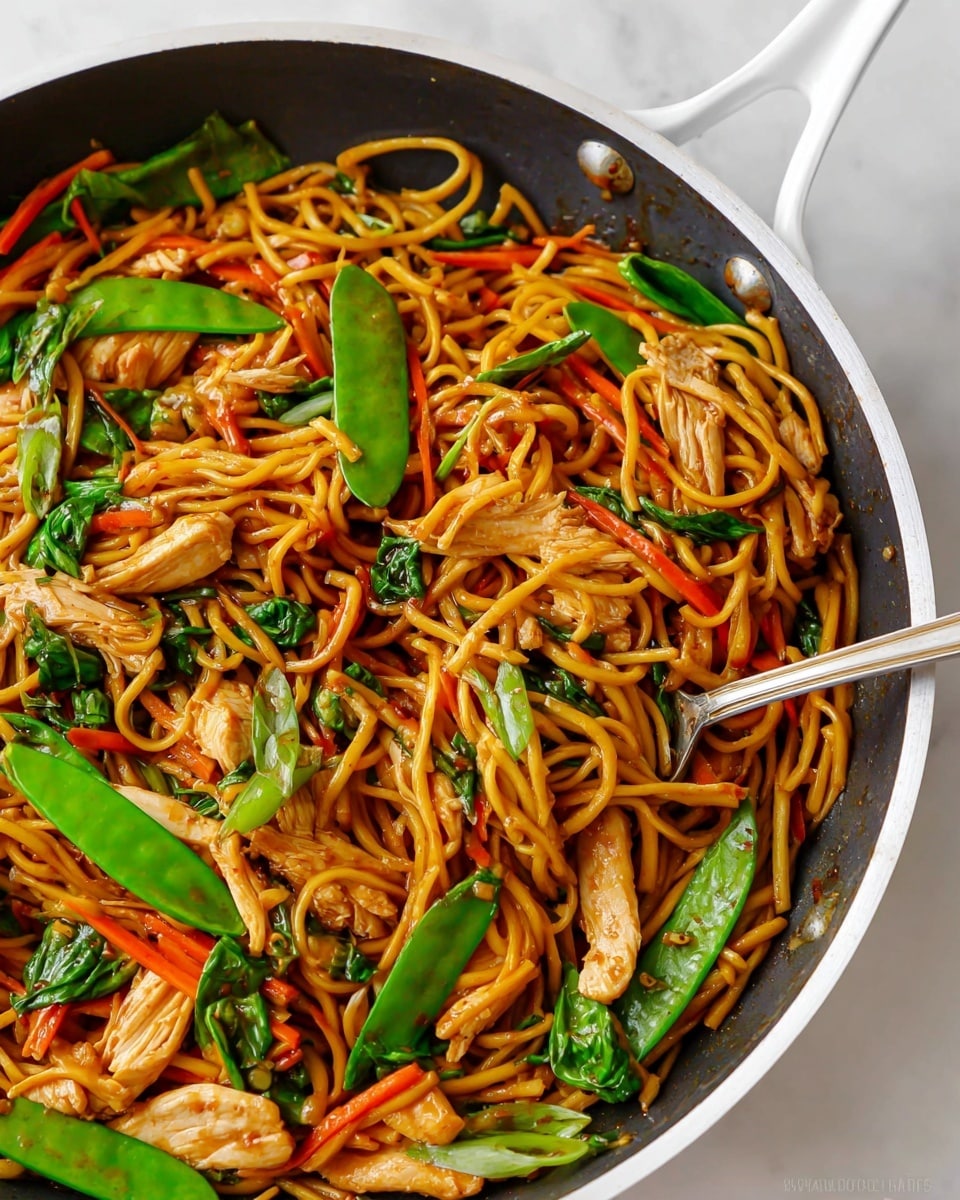 Large white skillet filled with a whole serving of vibrant chicken chow mein noodles, featuring tender strips of chicken, bright green snap peas, thin carrot sticks, and fresh leafy greens, all tossed in a glossy savory sauce, garnished with hints of fresh herbs, shot from a 3/4 angle with the entire skillet in frame, resting on a white marble countertop with natural lighting, professional food styling photo taken with an iphone --ar 4:5 --v 7