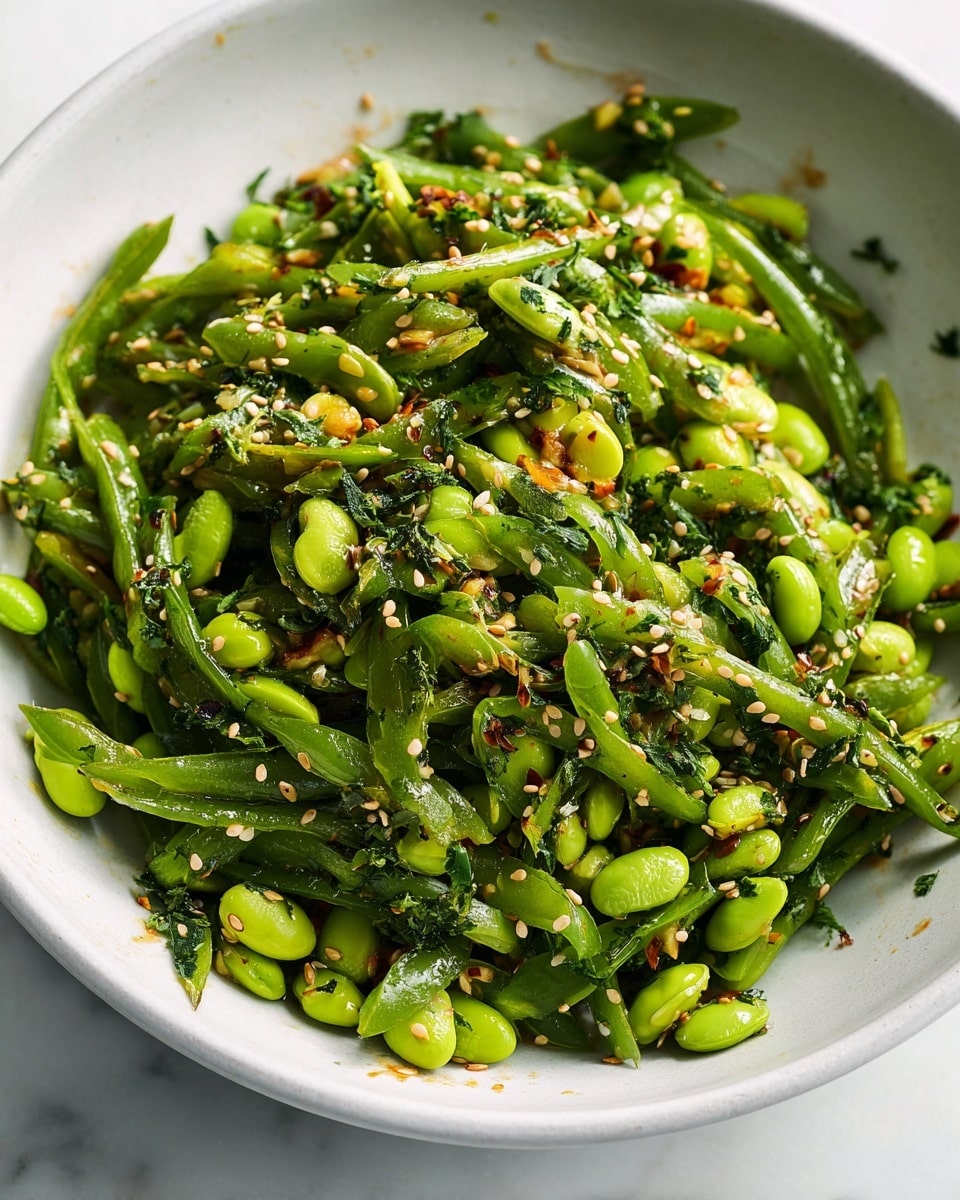 Large white bowl filled with a vibrant edamame and snap pea salad tossed in a spicy chili sesame dressing, garnished with fresh scallions, chopped herbs, and sprinkled sesame seeds, all ingredients glistening under natural light, whole dish shown from a 3/4 angle on a white marble surface, styled like a hero shot from a food magazine, photo taken with an iphone --ar 4:5 --v 7
