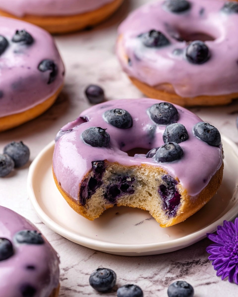 Multiple freshly baked donuts with smooth, glossy purple blueberry glaze evenly coating each one, arranged neatly on a white wire cooling rack over a white marble countertop, showcasing the entire batch of perfectly round donuts with subtle blueberry specks in the glaze, natural lighting highlighting the shiny finish, styled as a professional food magazine hero shot, photo taken with an iphone --ar 4:5 --v 7