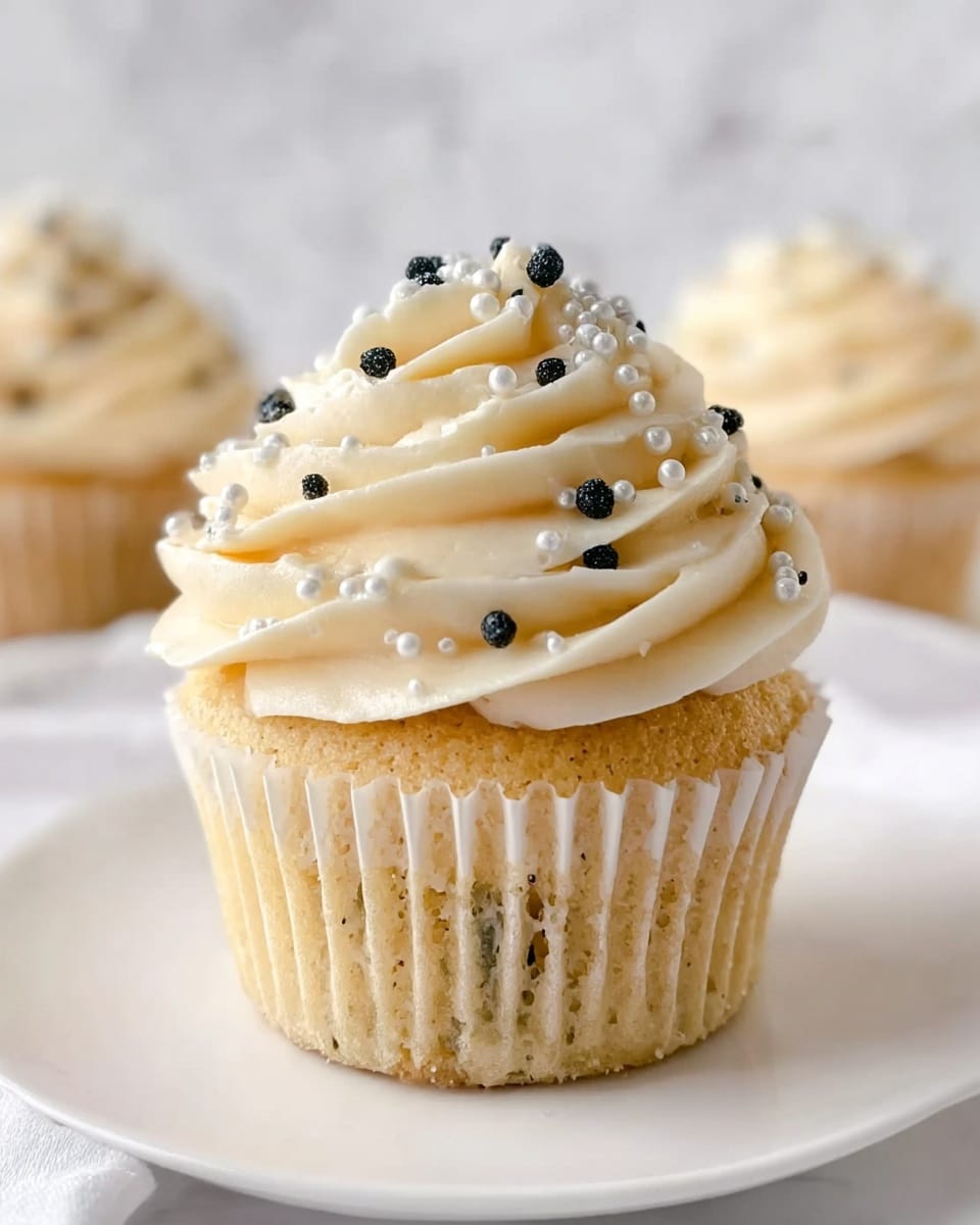 A pristine white serving tray filled with a full dozen of vanilla cupcakes, each topped with a generous swirl of creamy white buttercream frosting, adorned with an elegant mix of small white sugar pearls and glossy silver dragees. The cupcakes are uniformly arranged, showcasing their fluffy texture and uniform decoration, shot at a professional 3/4 angle on a white marble surface with natural lighting, highlighting the delicate details and inviting appearance of the entire assortment, photo taken with an iphone --ar 4:5 --v 7