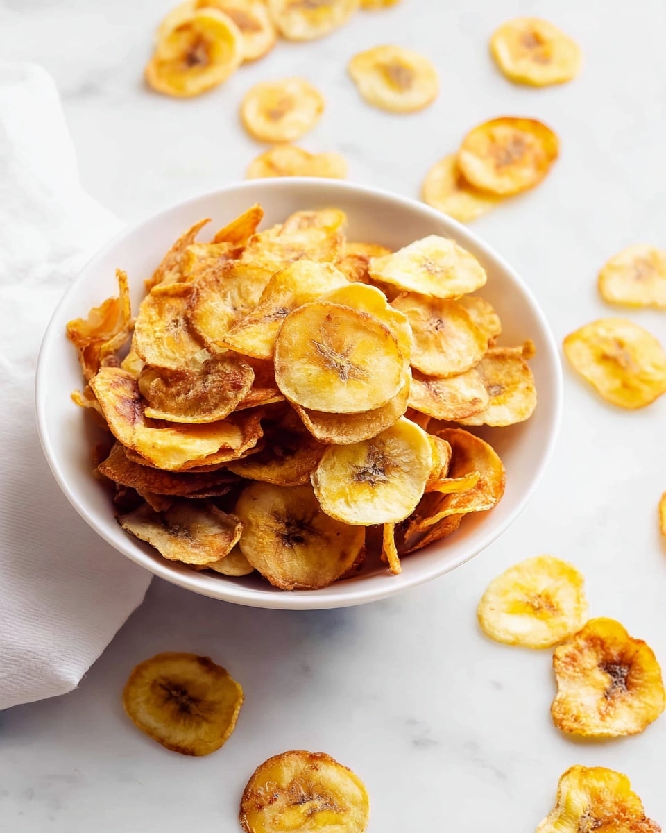 Large white bowl filled with a generous serving of crisp, golden banana chips, heaped high and surrounded by scattered chips on a pristine white marble countertop, natural lighting highlighting the crunchy texture and warm yellow hues, professional overhead food magazine style photo taken with an iphone --ar 4:5 --v 7